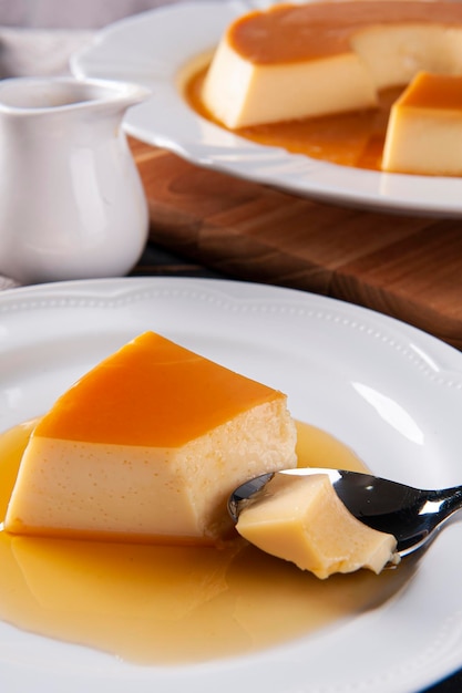 Delicious condensed milk pudding on white plate Someone scooping up a piece with a spoon