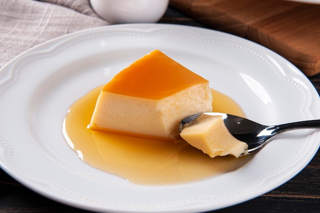 Delicious condensed milk pudding on white plate Someone scooping up a piece with a spoon