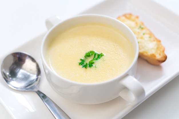 Delicious corn soup In a white bowl served with bread.