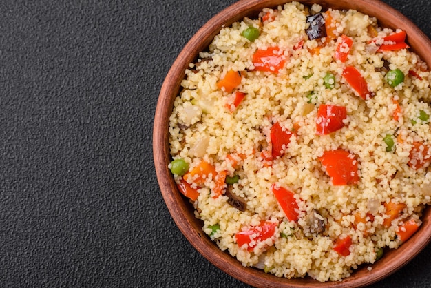 Delicious couscous porridge with cubes of grilled vegetables with salt and spices on a dark concrete background