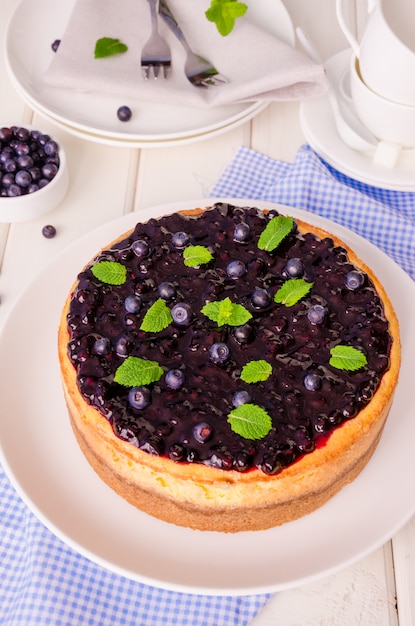 Delicious cream cheesecake with lemon zest and blueberry jam on a plate on a white wooden table