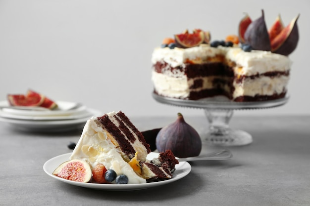 Delicious creamy cake with figs and berries on light grey background