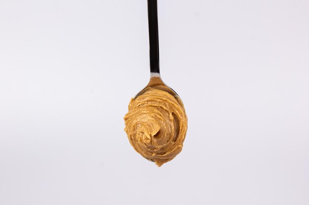 Delicious creamy peanut butter is laid out in a beautiful slide in a spoon on a white background Tasty breakfast Healthy food concept