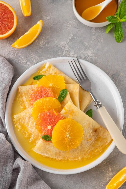 Delicious crepes suzette with orange syrup and slices fruits on a plate top view