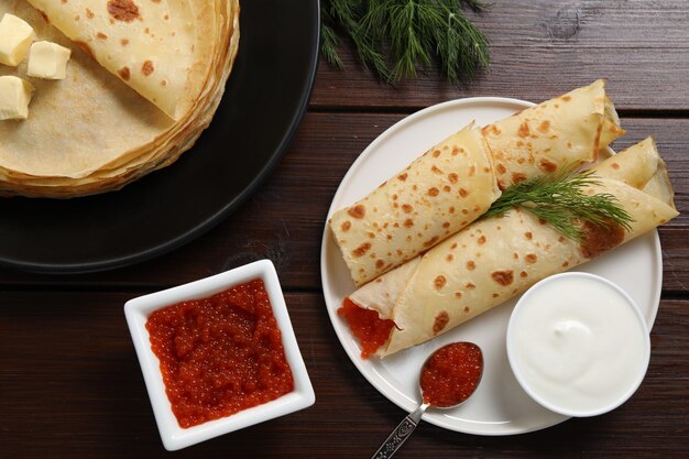 delicious crepes with red caviar served on wooden table flat lay