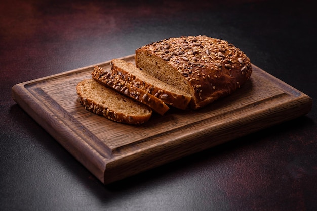 Delicious crispy bread with cereals on a wooden cutting board on a dark concrete background