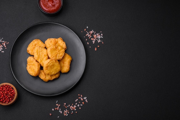 Delicious crispy chicken nuggets with salt and spices on a dark concrete background