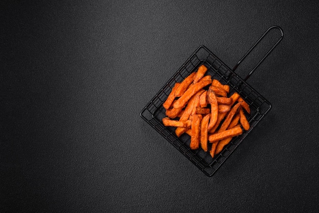 Delicious crispy sweet potato fries with salt spices and herbs on a dark concrete background