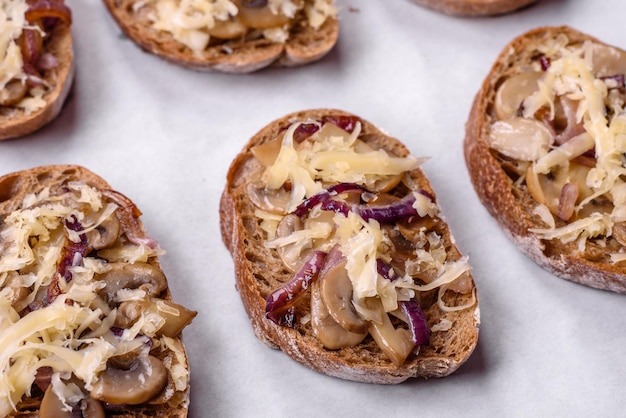 Delicious crispy toast or bruschetta with fried onion champignon mushrooms and cheese with spices and herbs on a dark concrete background