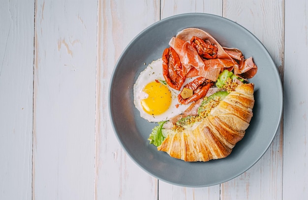 Delicious croissant breakfast stuffed with ricotta and avocado with sundried tomatoes pieces of jamon fried egg
