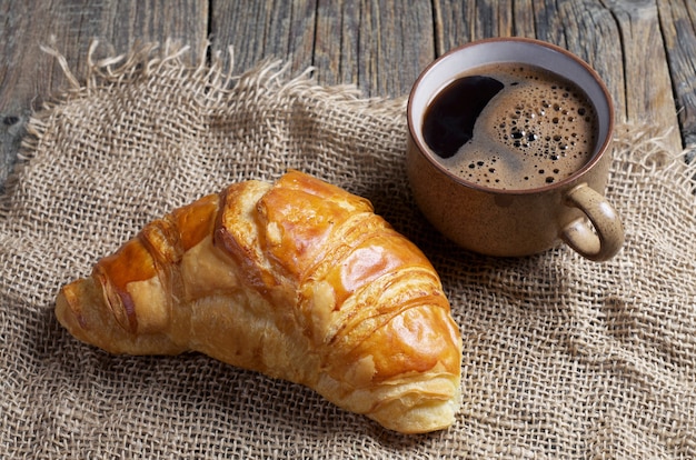 Delicious croissant and cup of coffee on the wooden table