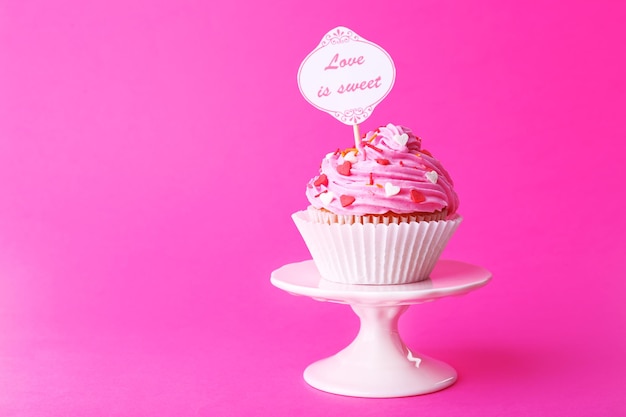 Delicious cupcake with inscription on pink background