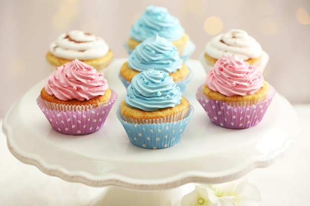 Delicious cupcakes on cake stand on table on light background