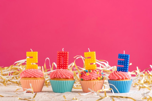 Delicious cupcakes decorated with candles in form of numbers 2023 on pink background New Years Eve Celebration