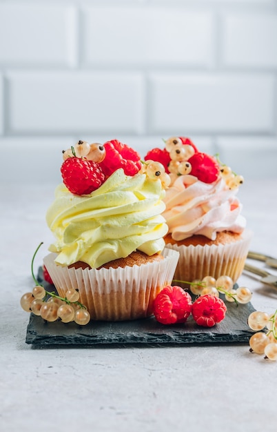 Delicious cupcakes with fresh raspberries and currants on black slate over light beige background. Selective focus