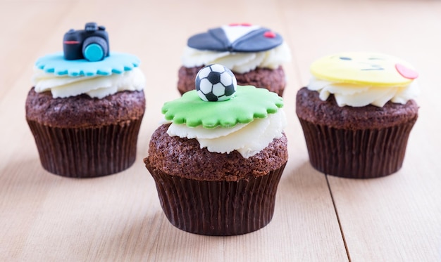 Delicious cupcakes with icons of ball tuxedo smiley and camera on it on wooden desk