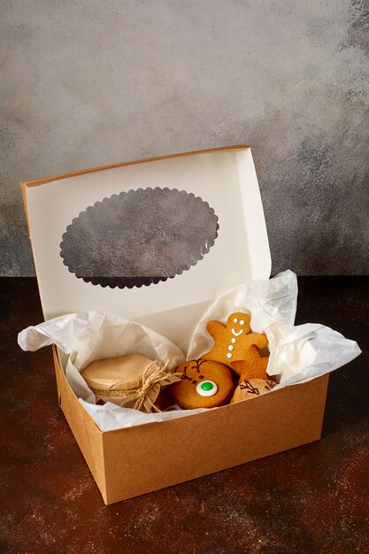 Photo delicious curly christmas gingerbread, caramel in a jar covered with paper and tied with string, chocolate in a package in a gift box