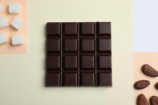 Delicious dark chocolate bar refined sugar and cocoa beans on color background flat lay