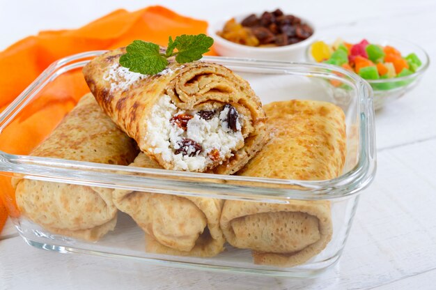 Delicious delicate pancakes with cottage cheese and raisins in a glass container on a white wooden background.  Close up