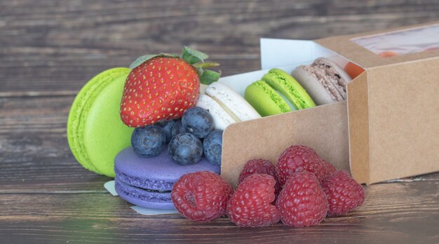 Foto deliziosi amaretti di colore diverso e frutti di bosco con fragole su una superficie di legno