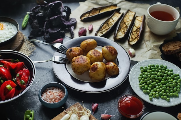 Delicious dinner table for two with fried potatoes organic tomatoes salad olives green onion eggplants eggs on dark stone background Healthy food concept various food and snacks