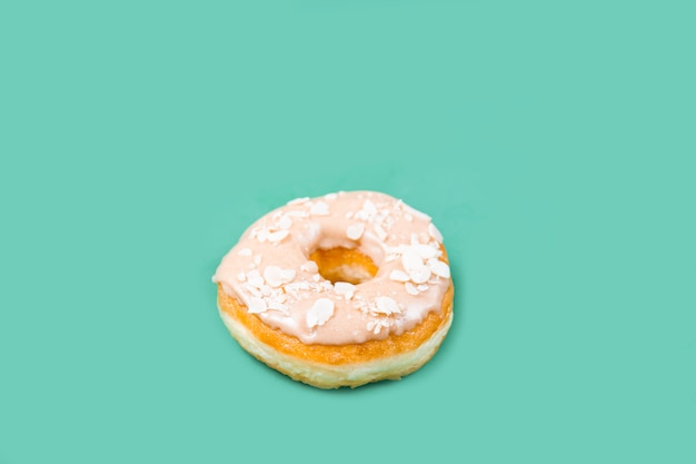 Delicious donut with glaze and almond crumbs close-up on a green table. Sweet food (dessert) concept.