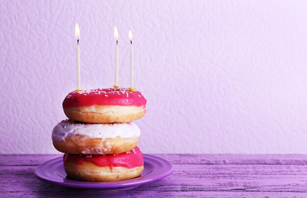 Delicious donuts with icing and birthday candles on table on light background