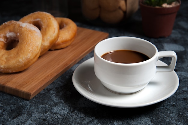 Delicious donuts with icing and cup of coffee in plate on black marble table.