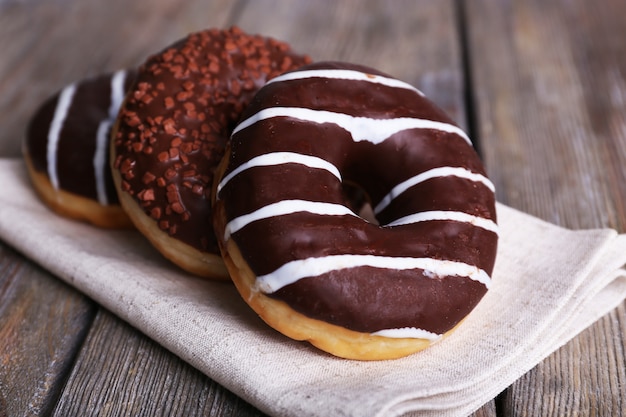 Delicious donuts with icing on napkin on wooden table