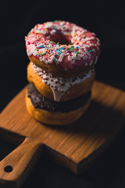 Delicious donuts on wooden board placed on wooden cutting board on black background