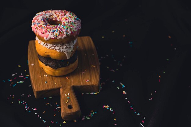 Delicious donuts on wooden board placed on wooden cutting board on black background