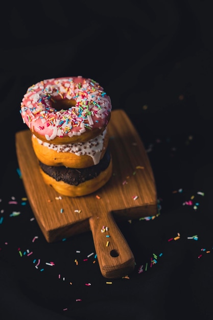 Delicious donuts on wooden board placed on wooden cutting board on black background