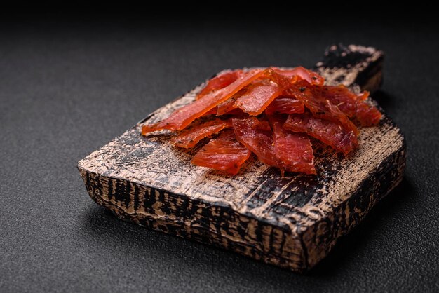 Delicious dried veal or turkey jerky with salt spices and herbs on a dark concrete background