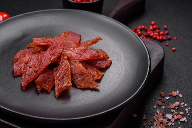 Delicious dried veal or turkey jerky with salt spices and herbs on a dark concrete background