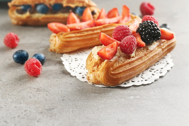 Delicious eclairs with berries and doily on table