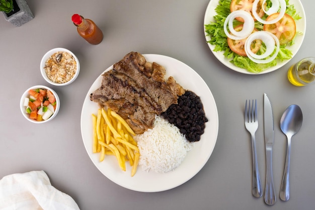 Delicious executive dish of beef steak rice beans french fries and green salad with lettuce tomato and onion accompanied by farofa and vinaigrette Typical Brazilian food Selective focus