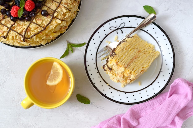 Delizioso dessert festivo a strati con pasta sfoglia e crema pasticcera decorata con frutti di bosco freschi e tazza di tè al limone