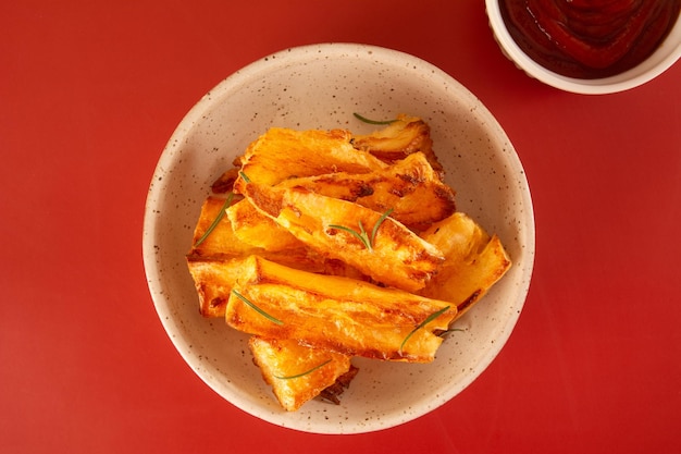 Delicious flatlay topview Fried Cassava in Handcrafted White Ceramic Bowl on Red Studio Background with Ketchup