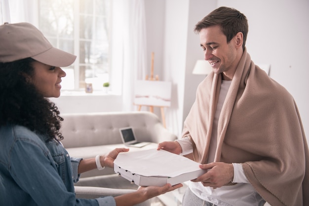 Delicious food. Joyful happy man looking at the delivery person while taking his pizza