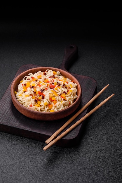 Delicious fresh Asian noodles with pieces of vegetables meat with salt spices and herbs on a dark concrete background