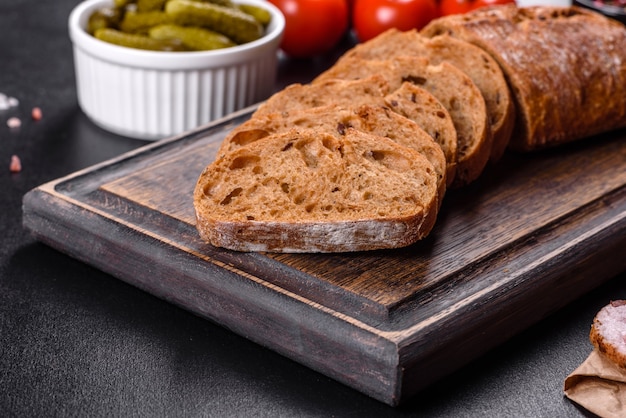 Deliziosa pancetta fresca affettata con pane e verdure su uno sfondo di cemento scuro