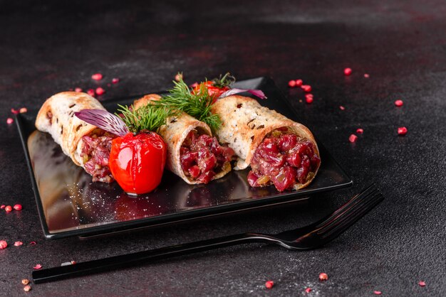 Delicious fresh beef tartar with toasts on a black square plate against a dark surface