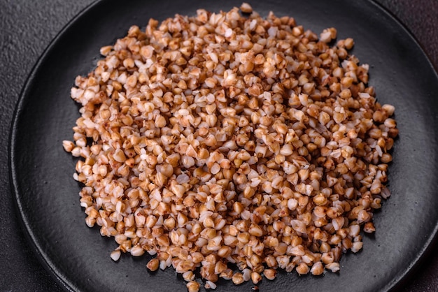 Delicious fresh boiled buckwheat porridge with vegetables and spices on a black plate