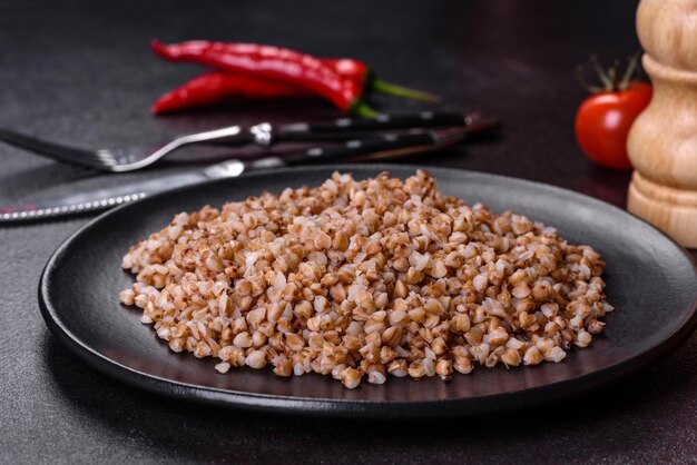 Delicious fresh boiled buckwheat porridge with vegetables and spices on a black plate