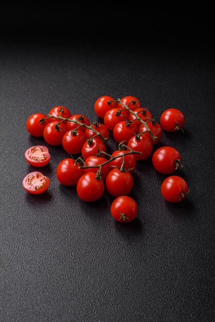 Delicious fresh cherry tomatoes on the branches as an ingredient for cooking a vegetarian dish on a dark concrete background