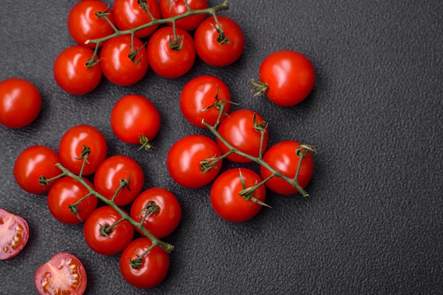 Delicious fresh cherry tomatoes on the branches as an ingredient for cooking a vegetarian dish on a dark concrete background