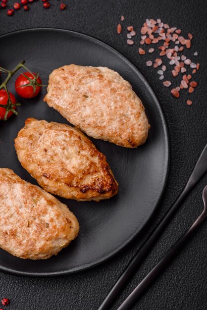 Delicious fresh chicken cutlets or meatballs with salt spices and herbs on a dark concrete background