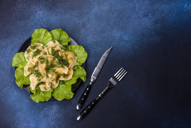 Delicious fresh cooked dumplings with potatoes embellished with greens and lettuce leaves on a dark plate