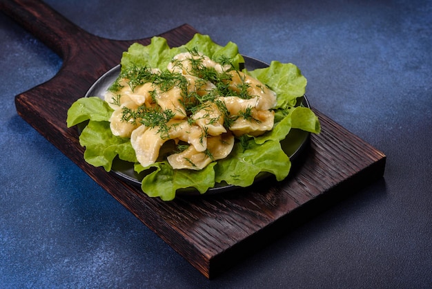 Delicious fresh cooked dumplings with potatoes embellished with greens and lettuce leaves on a dark plate