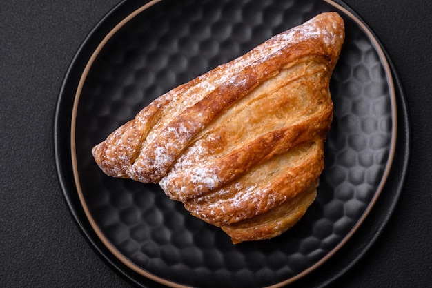 Delicious fresh crispy bun with jam on a black ceramic plate on a dark concrete background